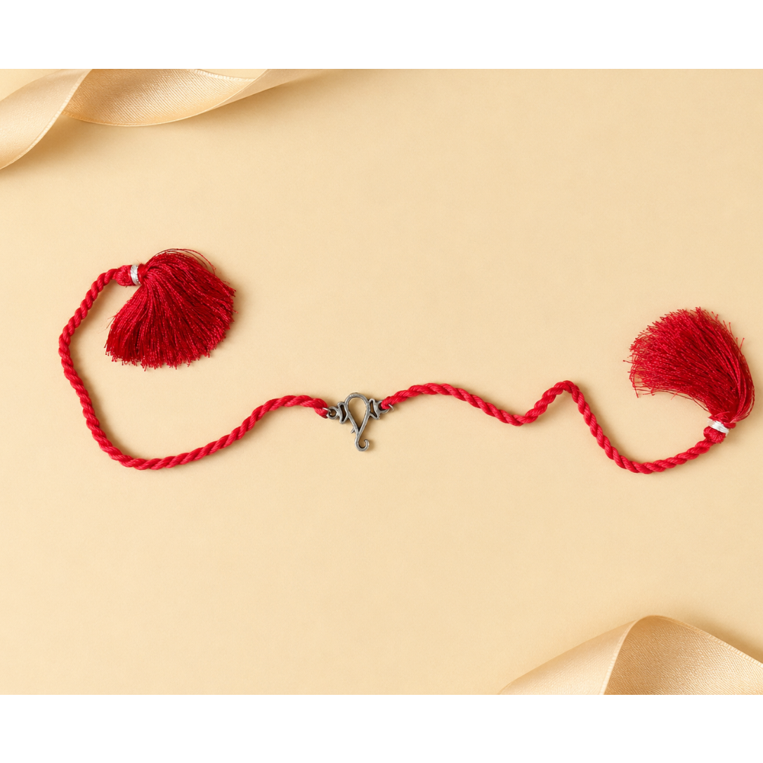 A red braided cord ornament with two red tassels and a small silver clasp, arranged on a warm beige background with soft cream ribbon curls in the corners.