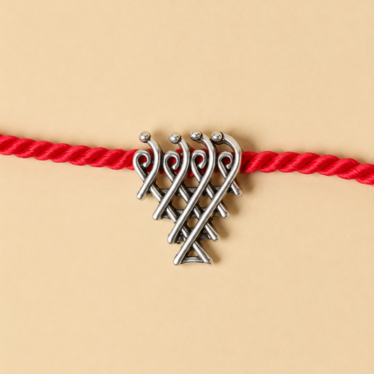A silver-toned metal knot charm with small bead accents, threaded onto a bright red braided cord, shown against a warm beige background.