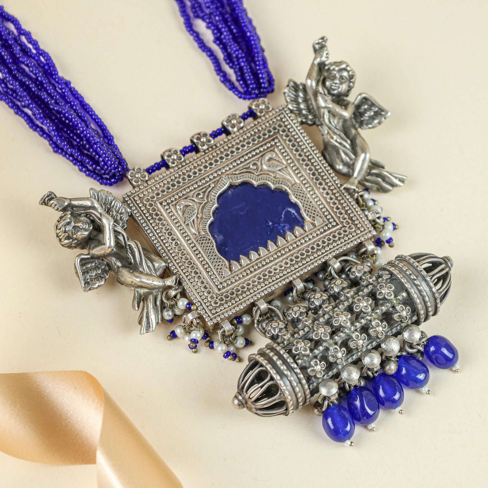 Decorative necklace with blue beads and silver pendant on a beige background