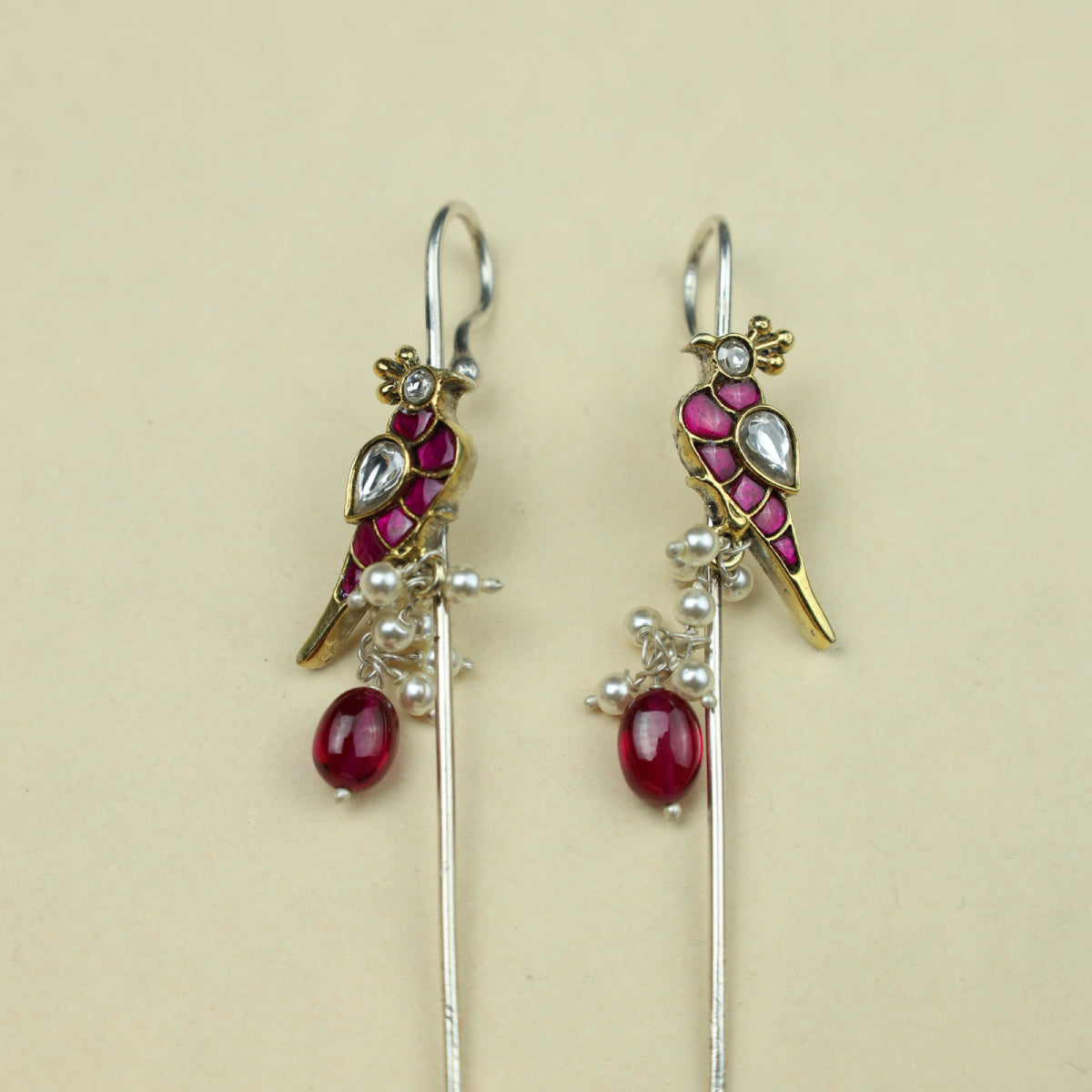 Pair of earrings with red gemstones and gold accents on a beige background