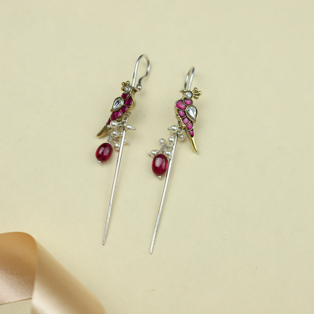 Pair of earrings with red gemstones and gold accents on a beige background
