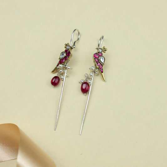 Pair of earrings with red gemstones and gold accents on a beige background