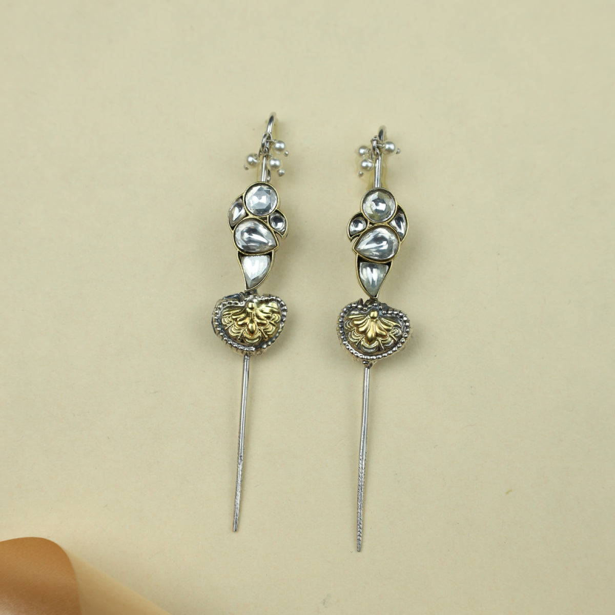 Pair of decorative earpins with gold and silver details on a beige background