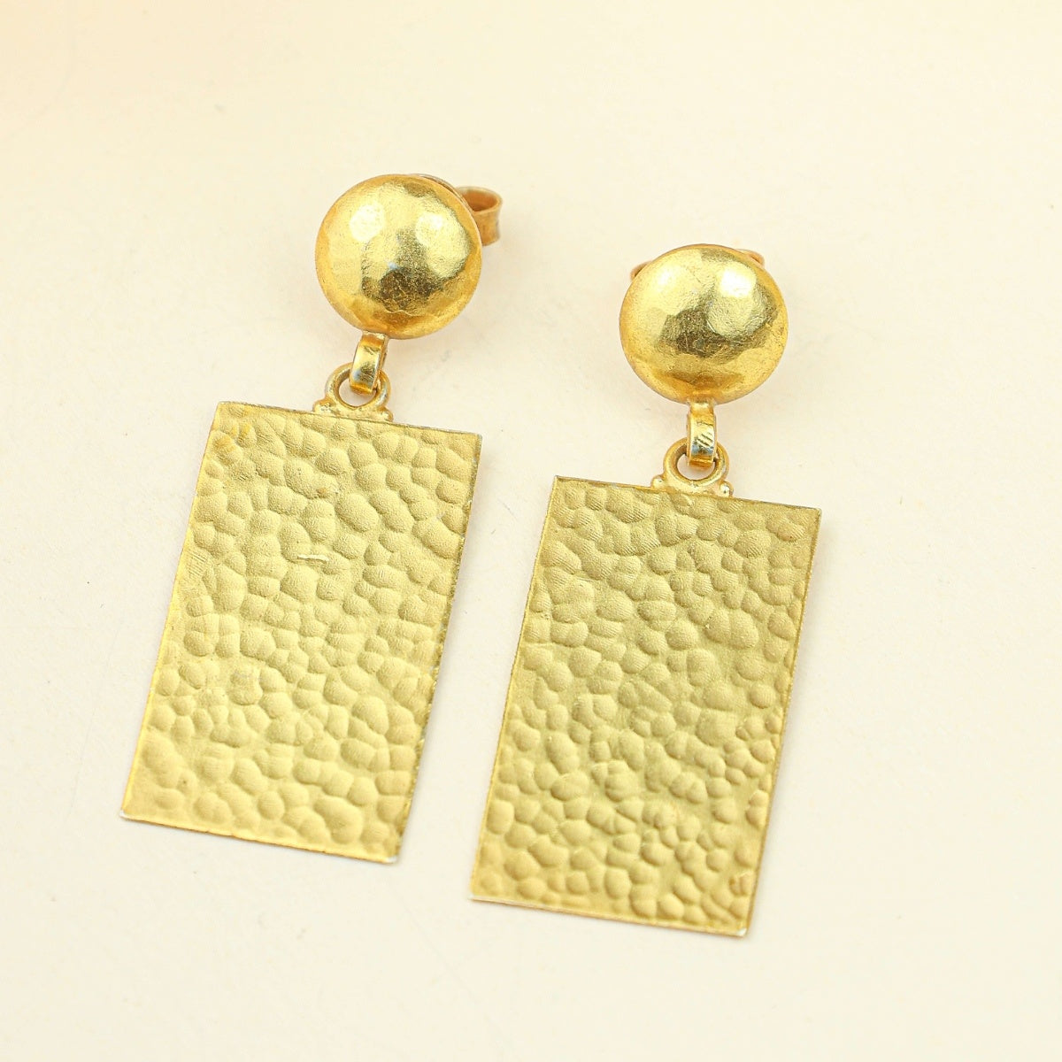 Gold earrings with textured rectangular pendants on a beige background