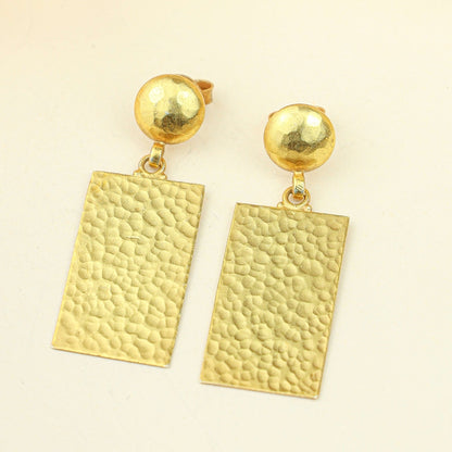Gold earrings with textured rectangular pendants on a beige background